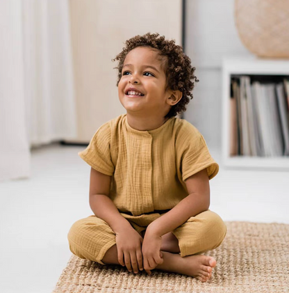 Toddler sitting and smiling wearing yellow breathable cotton romper indoors