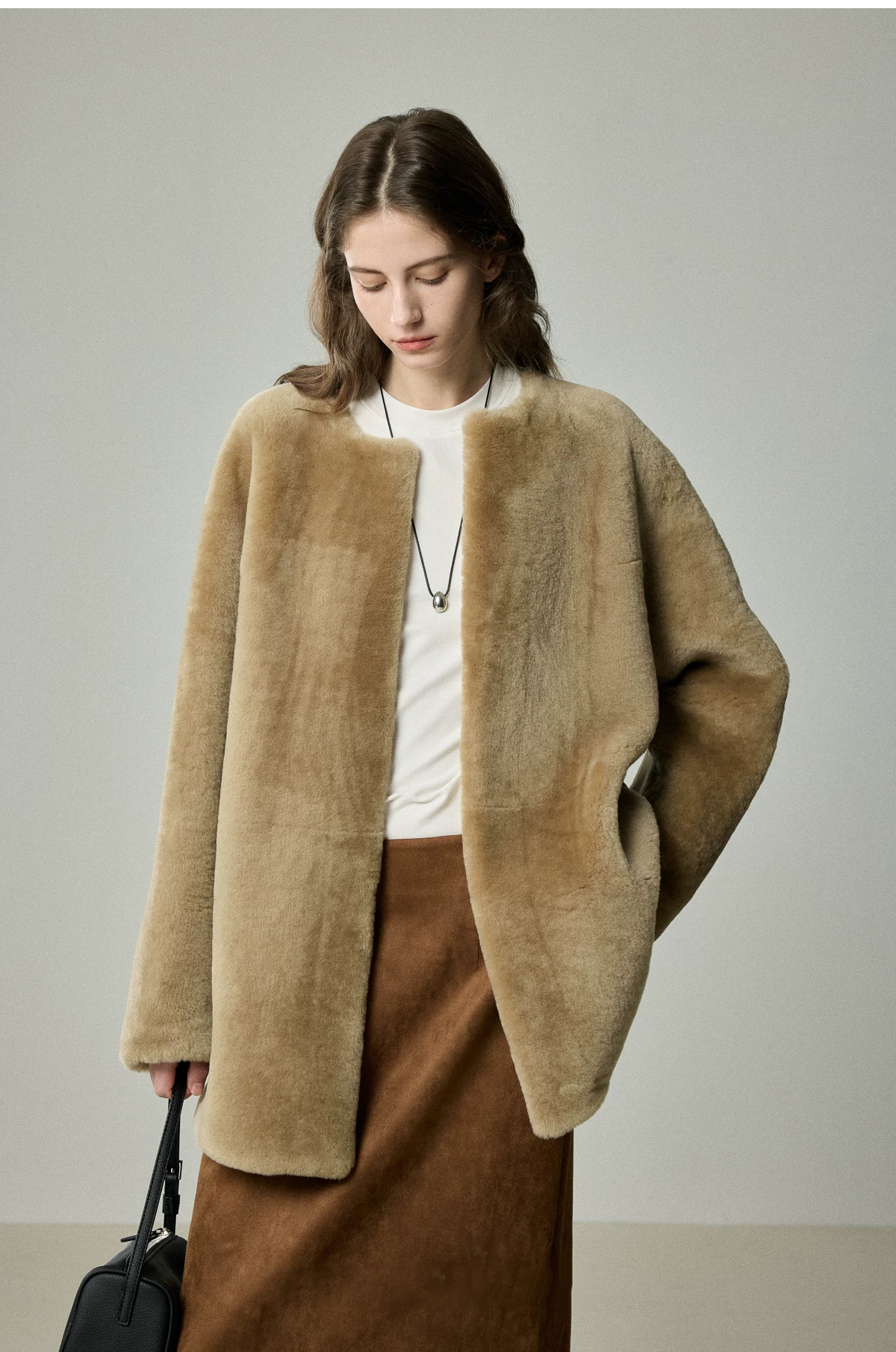 Camel sheepskin shearling jacket with collarless round neck worn open over a white tee and rust suede skirt