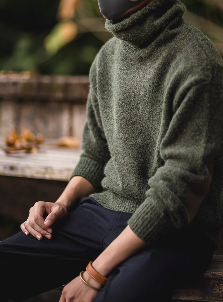 Man wearing Elbow Patch Turtleneck Sweater in olive green sitting outdoors highlighting soft knit fabric and comfortable casual styling
