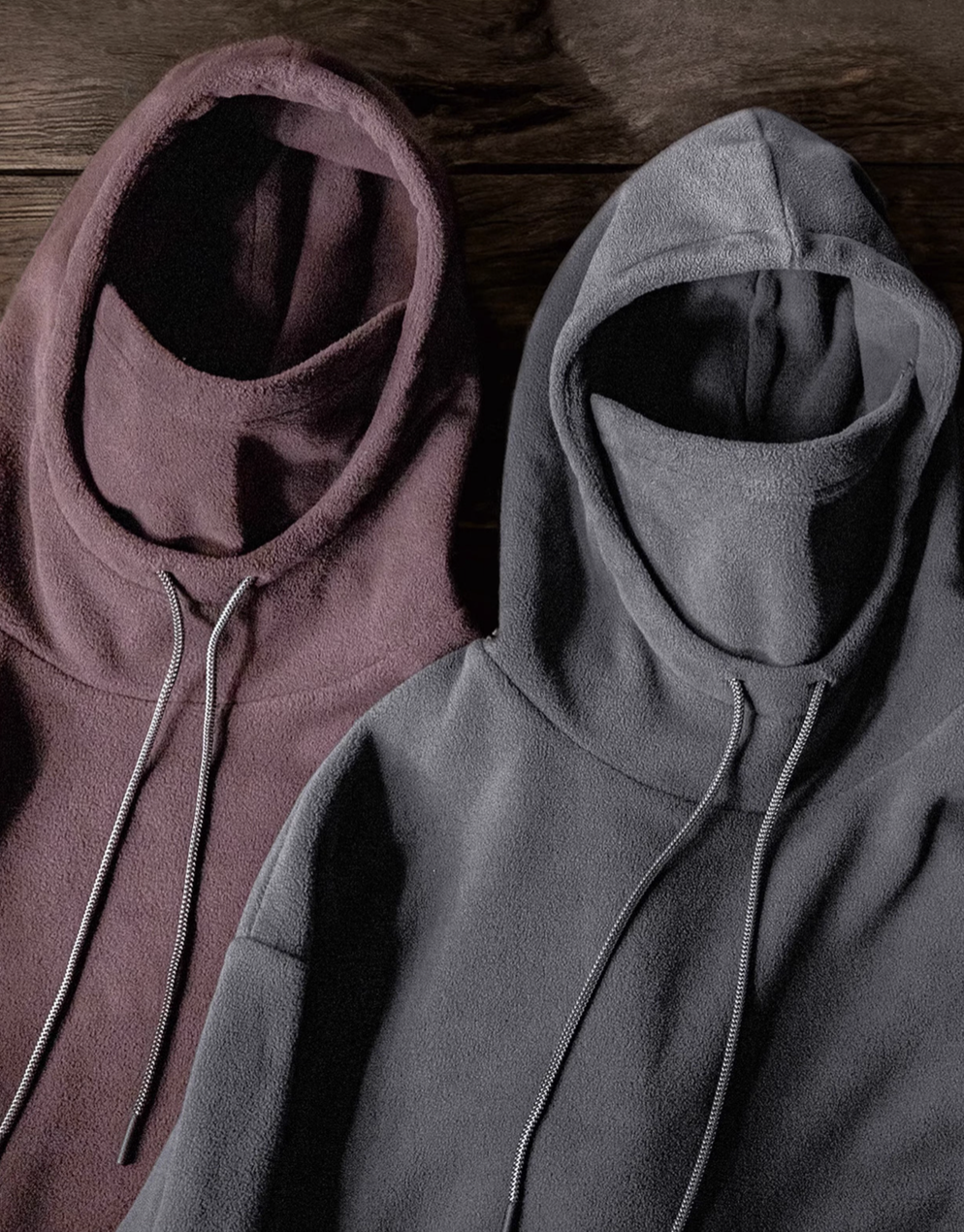 Elevate Shield Hoodie in dark gray and chestnut red displayed side by side showing fleece texture, visor hood, and integrated face guard design