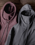 Elevate Shield Hoodie in dark gray and chestnut red displayed side by side showing fleece texture, visor hood, and integrated face guard design