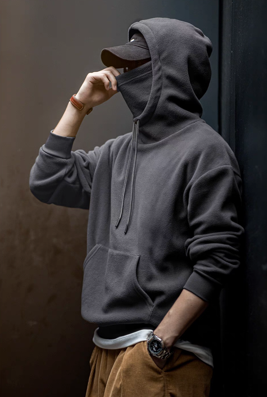 Man wearing Elevate Shield Hoodie in dark gray pulling up integrated face guard with visor hood for cold weather protection