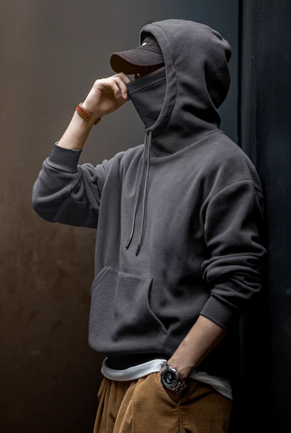 Man wearing Elevate Shield Hoodie in dark gray pulling up integrated face guard with visor hood for cold weather protection