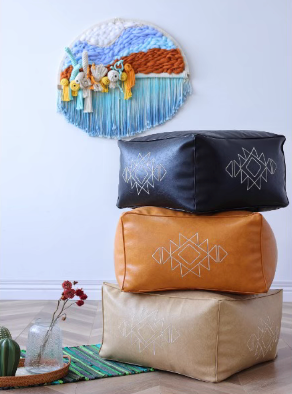 Stacked embroidered square bean bag sofas in black, orange yellow, and khaki with geometric patterns, styled in a living room with wall decor