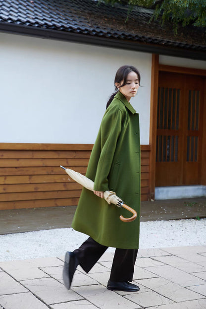 Army green wool overcoat side walking view with relaxed straight silhouette and minimalist design