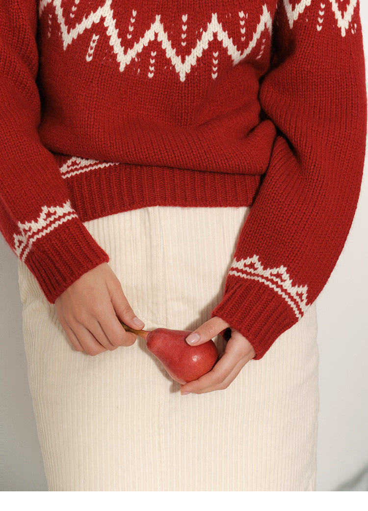 Detail of red Fair Isle merino wool sweater hem and cuffs with cream pattern, styled with an ivory corduroy skirt and a pear in the model’s hands.