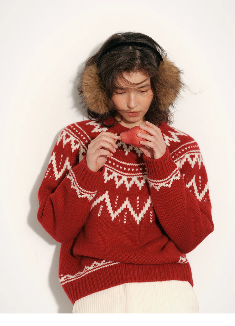 Woman looking down at a pear while wearing a red and cream Fair Isle merino wool sweater against a white background.
