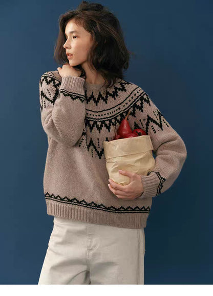 Side view of a woman in a taupe and black Fair Isle merino wool sweater holding a paper bag of red pears against a deep blue background.