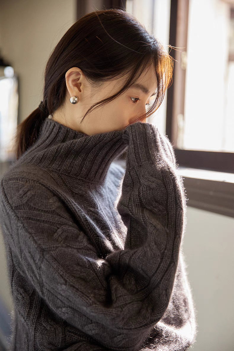 Close-up of dark gray cable-knit turtleneck sweater showcasing intricate knit texture and high ribbed collar