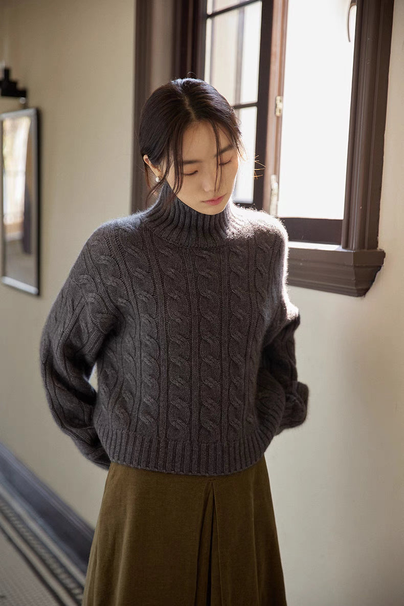 Dark gray cable-knit wool turtleneck sweater shown in soft window light highlighting textured knit and relaxed fit