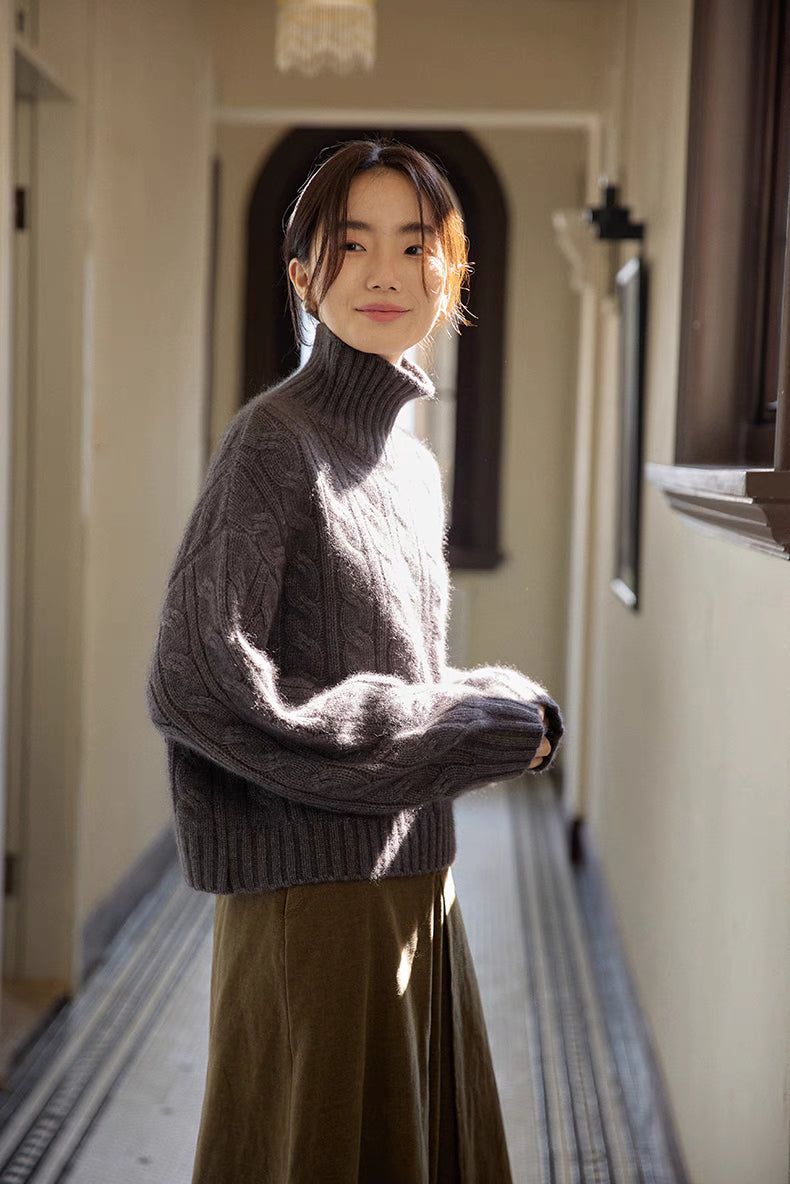 Dark gray cable-knit turtleneck sweater in side view with warm hallway lighting emphasizing cozy silhouette