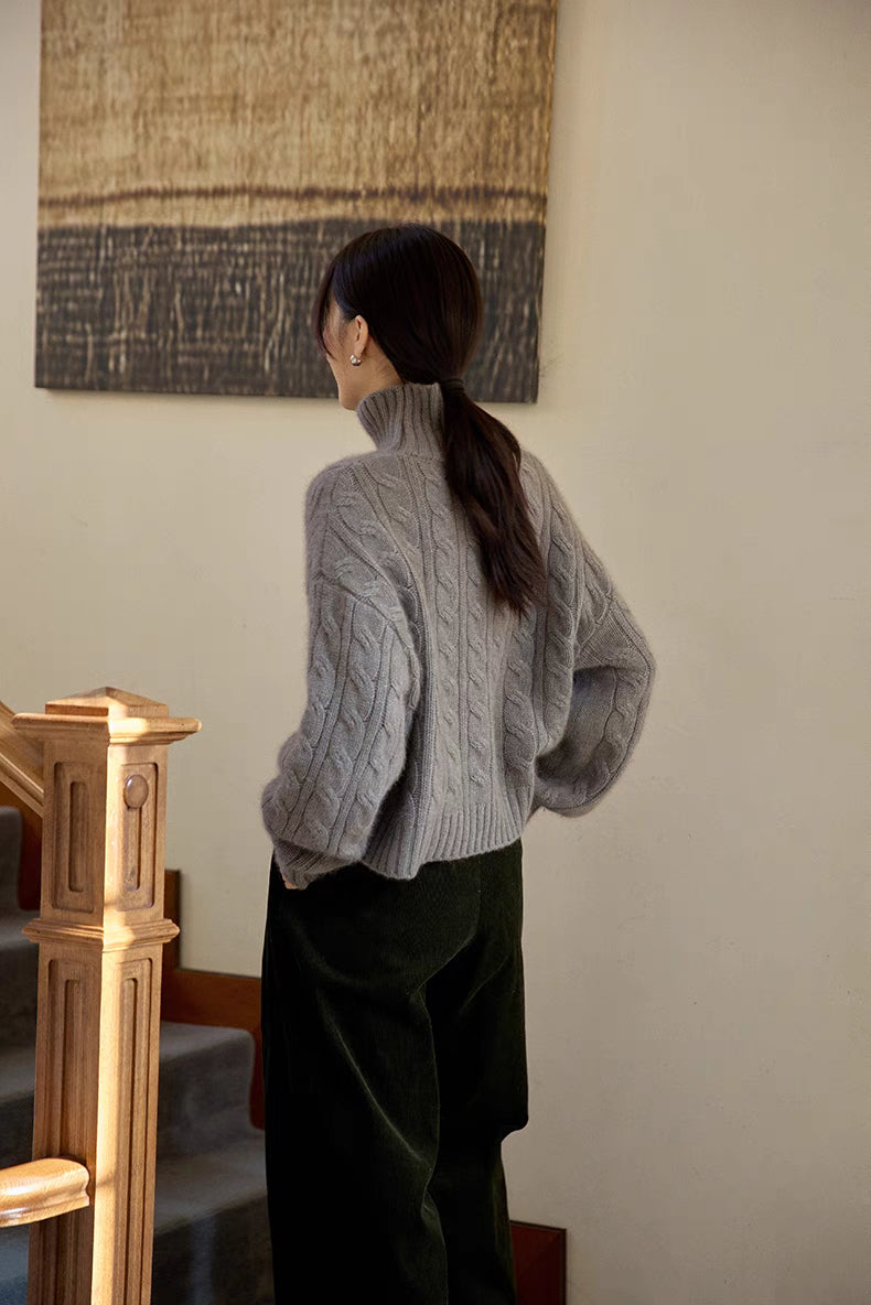 Back view of light gray cable-knit turtleneck sweater emphasizing knit detailing and relaxed silhouette