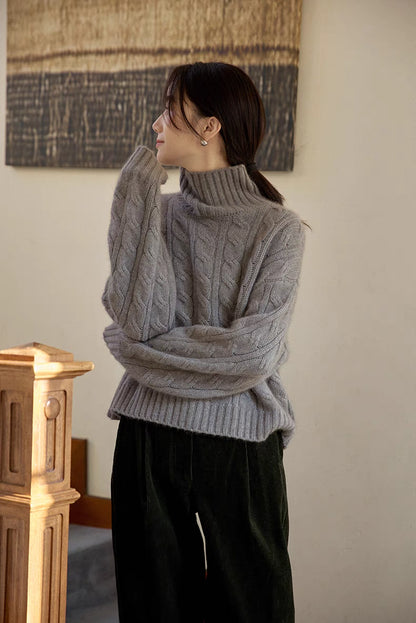 Light gray cable-knit wool turtleneck sweater displayed in soft indoor light highlighting texture and structure