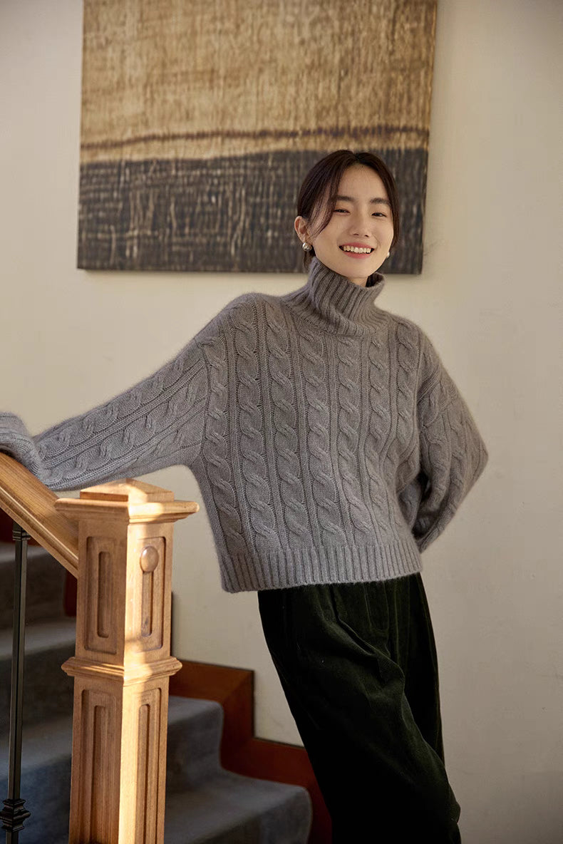 Light gray cable-knit sweater worn in relaxed pose near staircase showing cozy oversized fit