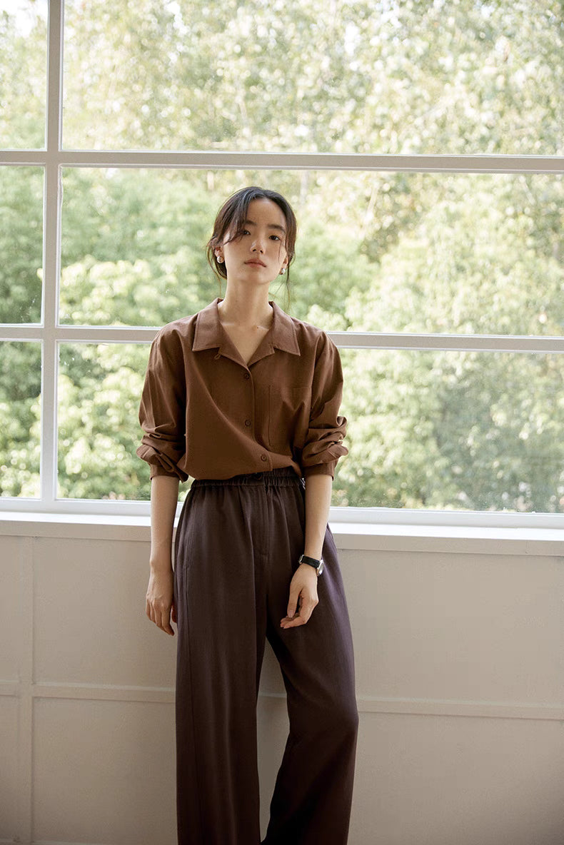 Woman wearing brown long-staple cotton button-up shirt full body front view, highlighting relaxed silhouette, button closure, and everyday styling