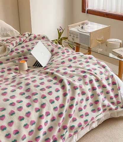 Strawberry fleece throw blanket spread across bed in cozy bedroom scene