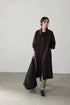 Model in a coffee brown fluid-drape Tencel trench coat, full front view, holding a large black tote bag.