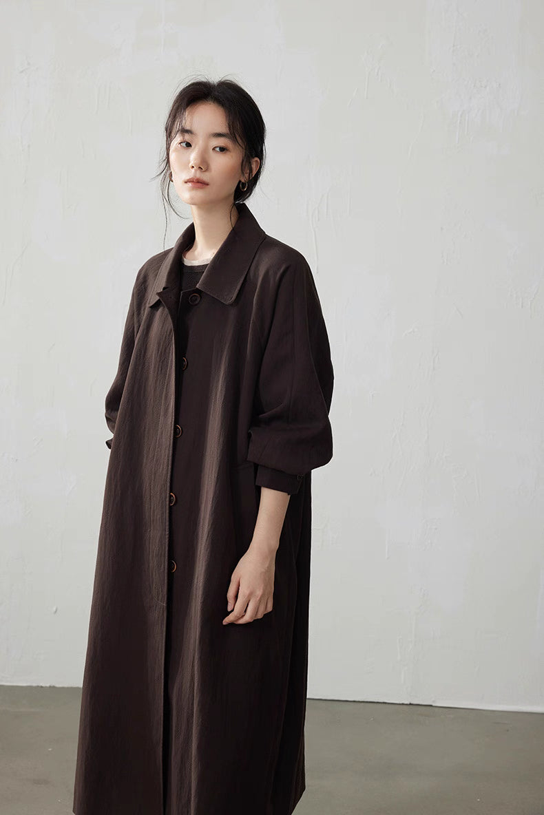 Close three-quarter front view of the coffee brown Tencel trench coat, showing relaxed straight silhouette and buttons.