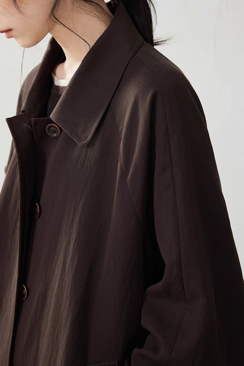 Detail shot of the coffee brown Tencel trench coat collar and corozo buttons, showing soft drape and subtle sheen.