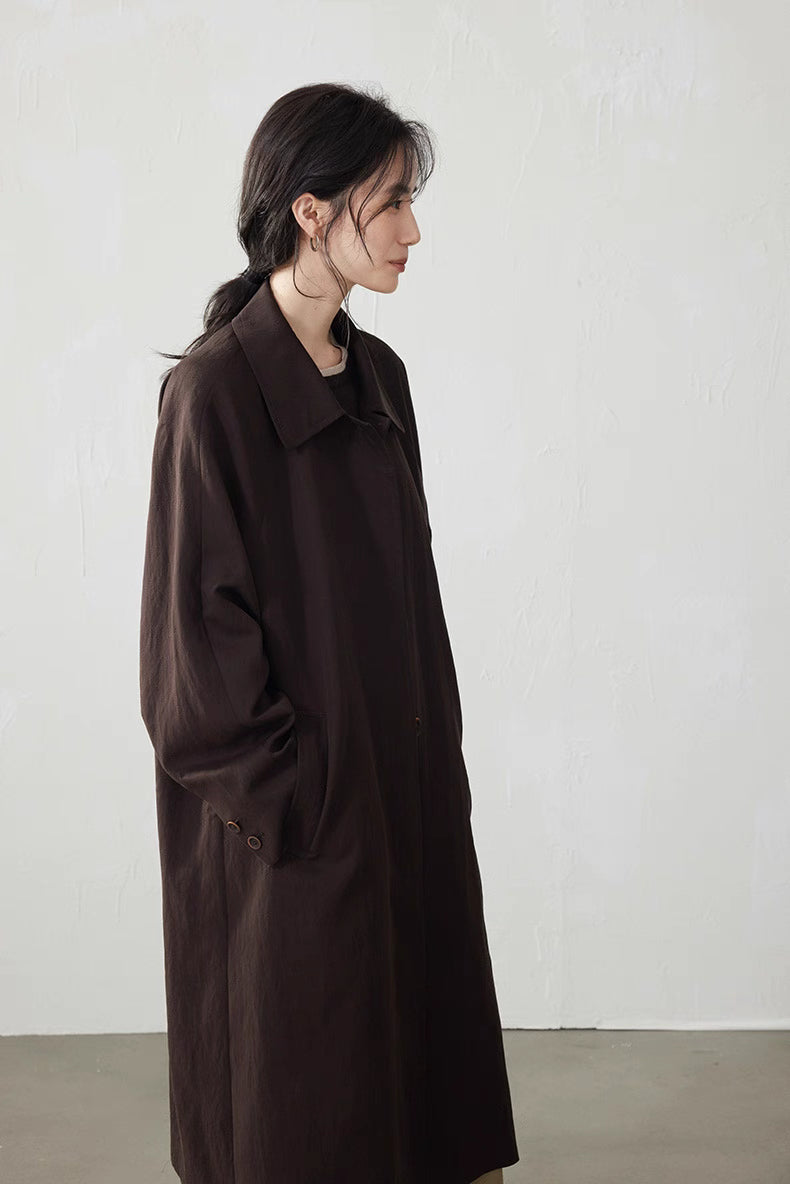 Side profile of the coffee brown fluid-drape Tencel trench coat, showing straight long line and pockets.