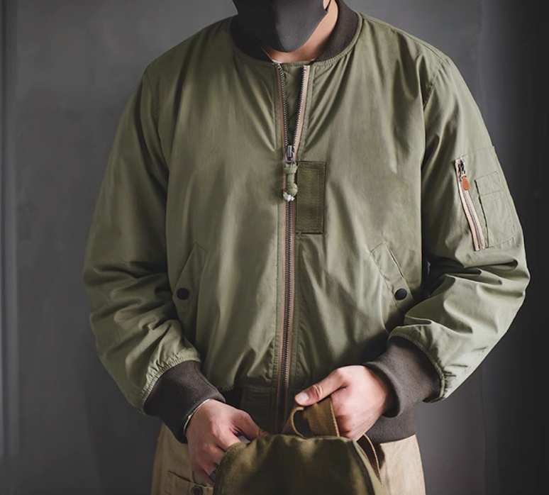 Model wearing army green MA-1 flight jacket with ribbed collar and zip sleeve pocket.