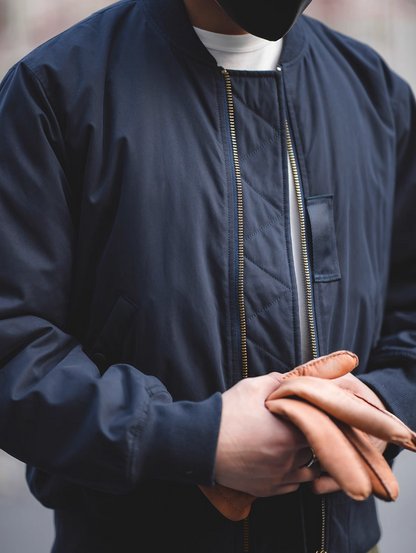 Model wearing deep navy MA-1 flight jacket with brown leather gloves and white tee.