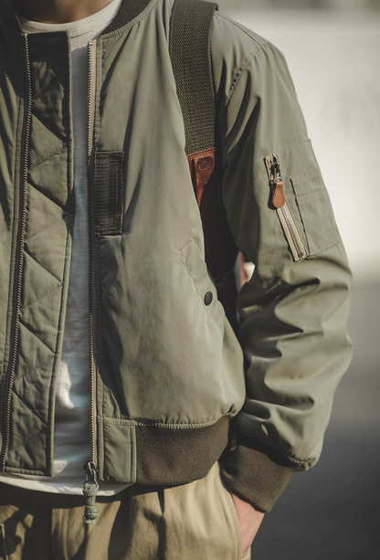 Model styling army green MA-1 bomber jacket outdoors with casual outfit.