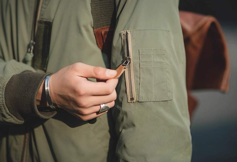 Close-up of utility sleeve zip pocket with leather zipper pull on MA-1 flight jacket.