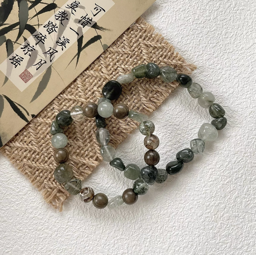 two forest spirit gemstone bracelets in green rutilated quartz green serpentine dzi beads and green rutilated quartz displayed together on textured surface
