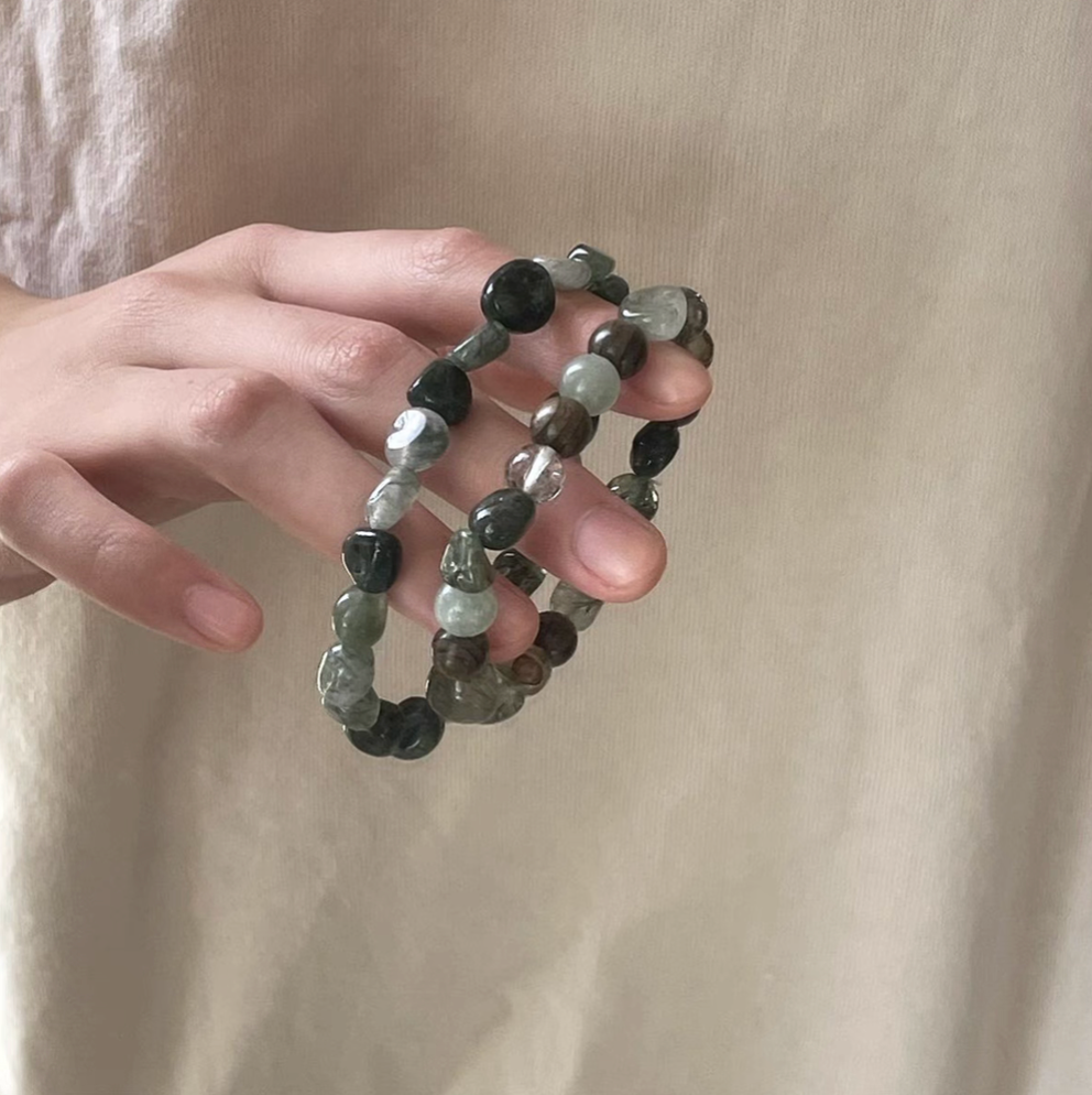 hand holding two forest spirit gemstone bracelets in green rutilated quartz green serpentine dzi beads and green rutilated quartz
