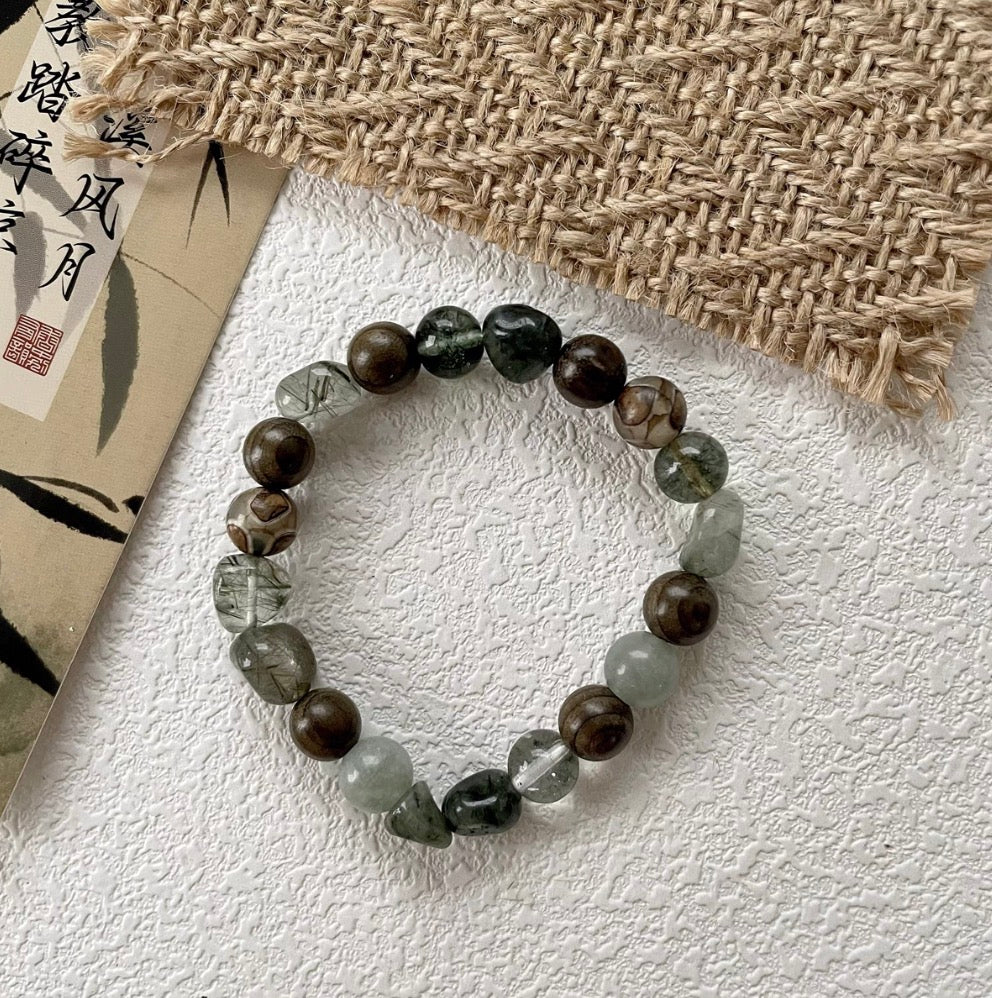 forest spirit gemstone bracelet in green rutilated quartz green serpentine and dzi beads displayed flat on textured background