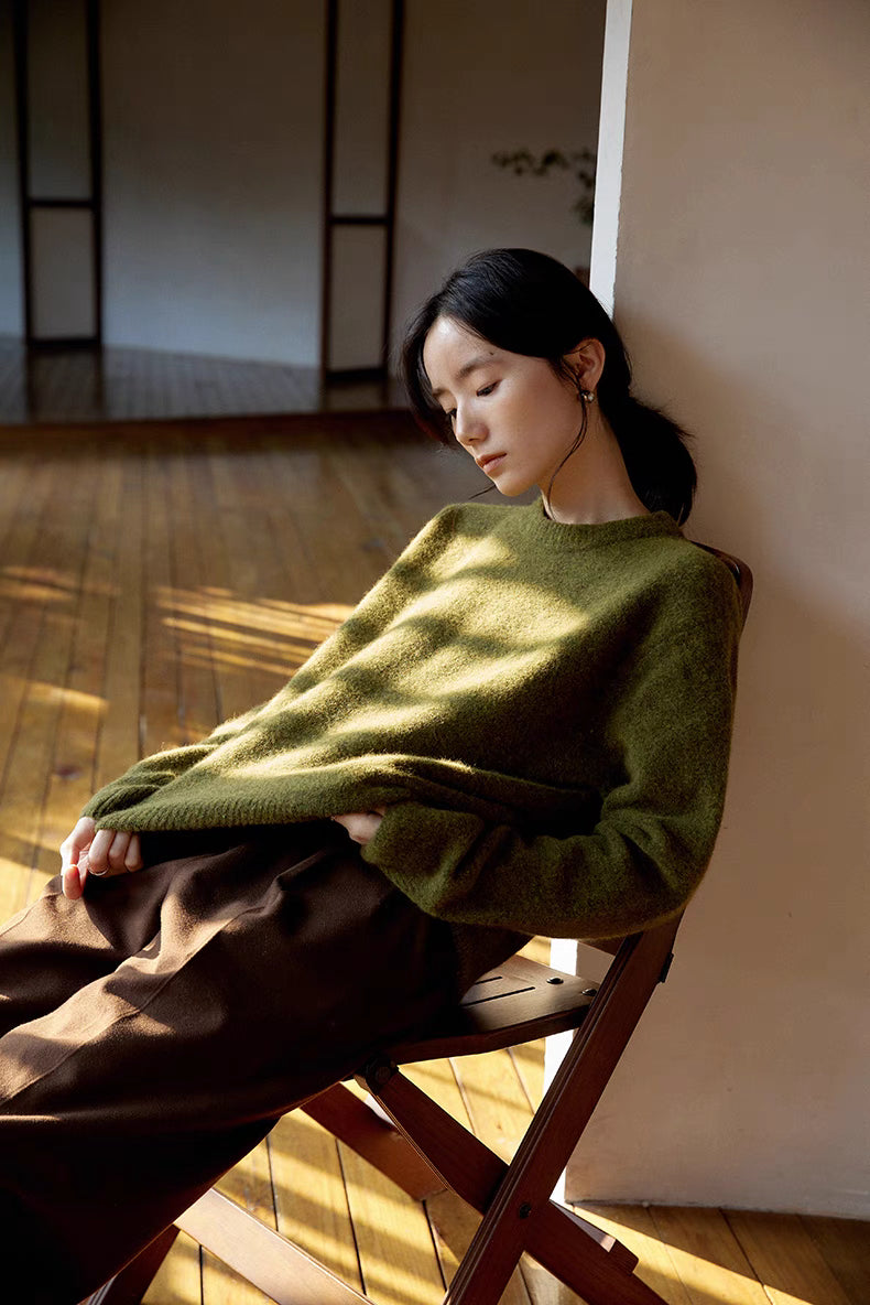 Cardamom green brushed wool sweater worn while leaning on chair with warm sunlight emphasizing plush knit