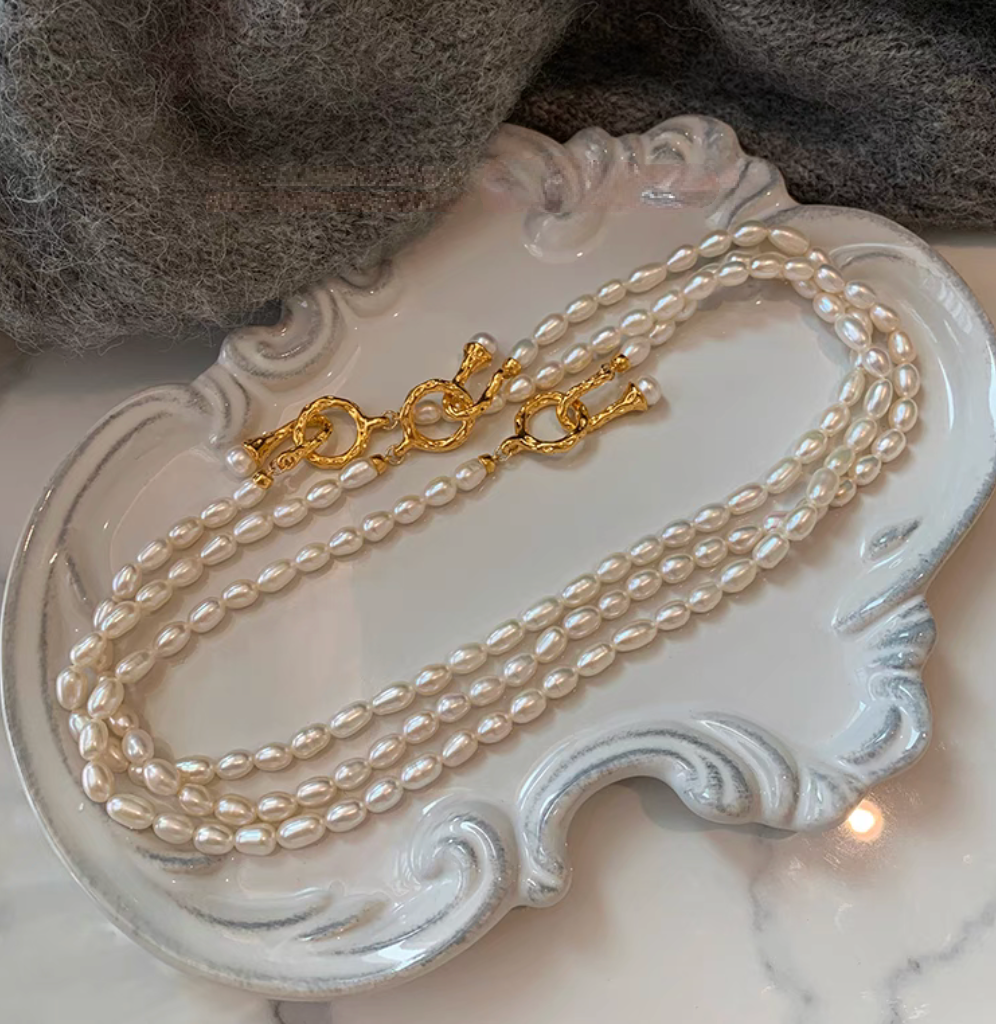 Multi-strand freshwater pearl choker necklaces with small oval pearls and decorative gold clasps arranged on ceramic tray