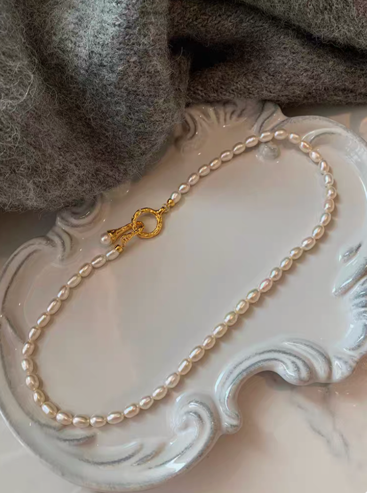 Single strand freshwater pearl choker necklace with small natural pearls and ornate gold clasp on decorative plate