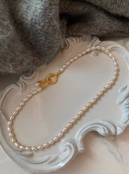 Single strand freshwater pearl choker necklace with small natural pearls and ornate gold clasp on decorative plate