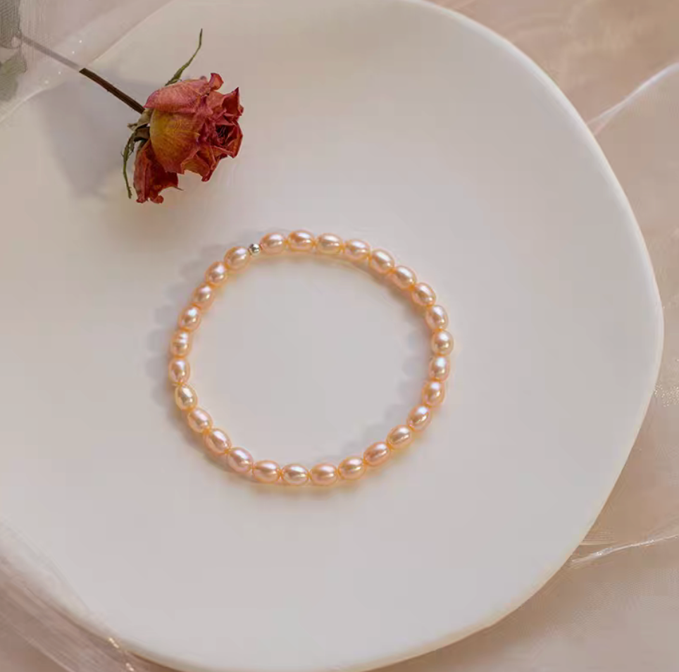 Flat lay of peachy pink freshwater pearl stretch bracelet arranged on plate with dried rose, warm and elegant tone.