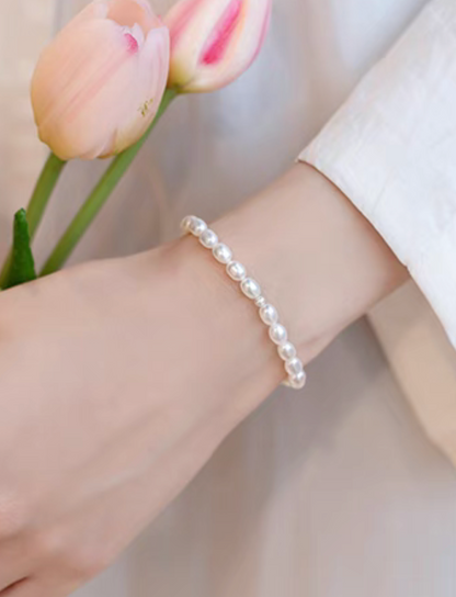 Lifestyle image of white freshwater pearl stretch bracelet worn on wrist, paired with soft neutral outfit and tulip background.