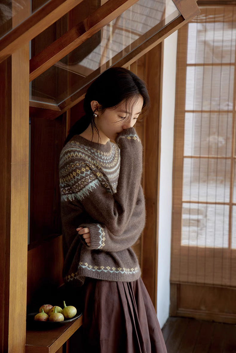 Model in smoky brown Frosted Peaks Fair Isle Sweater standing indoors near staircase with sleeve covering hand highlighting relaxed fit and cozy feel