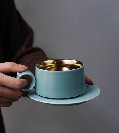Sky Blue Gold ceramic coffee mug held in hand, showcasing ring handle grip and gold interior with Lily of the Valley engraving