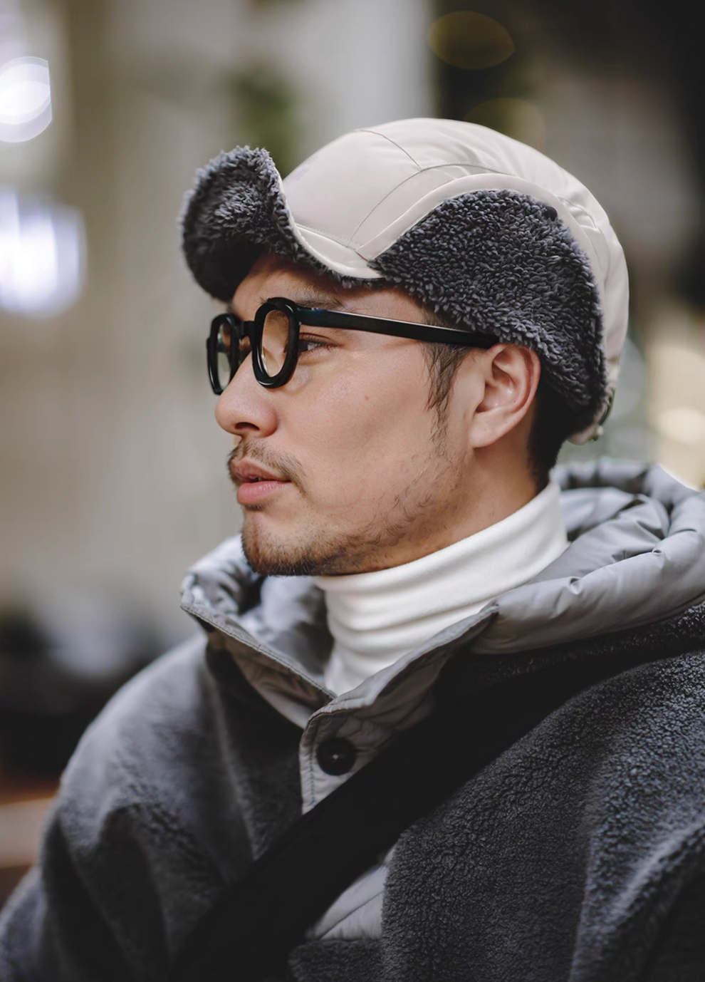 Man wearing Glacier Guard Fleece Cap mountain rock gray and white with ear flaps down showcasing soft sherpa lining warmth and winter-ready outdoor styling