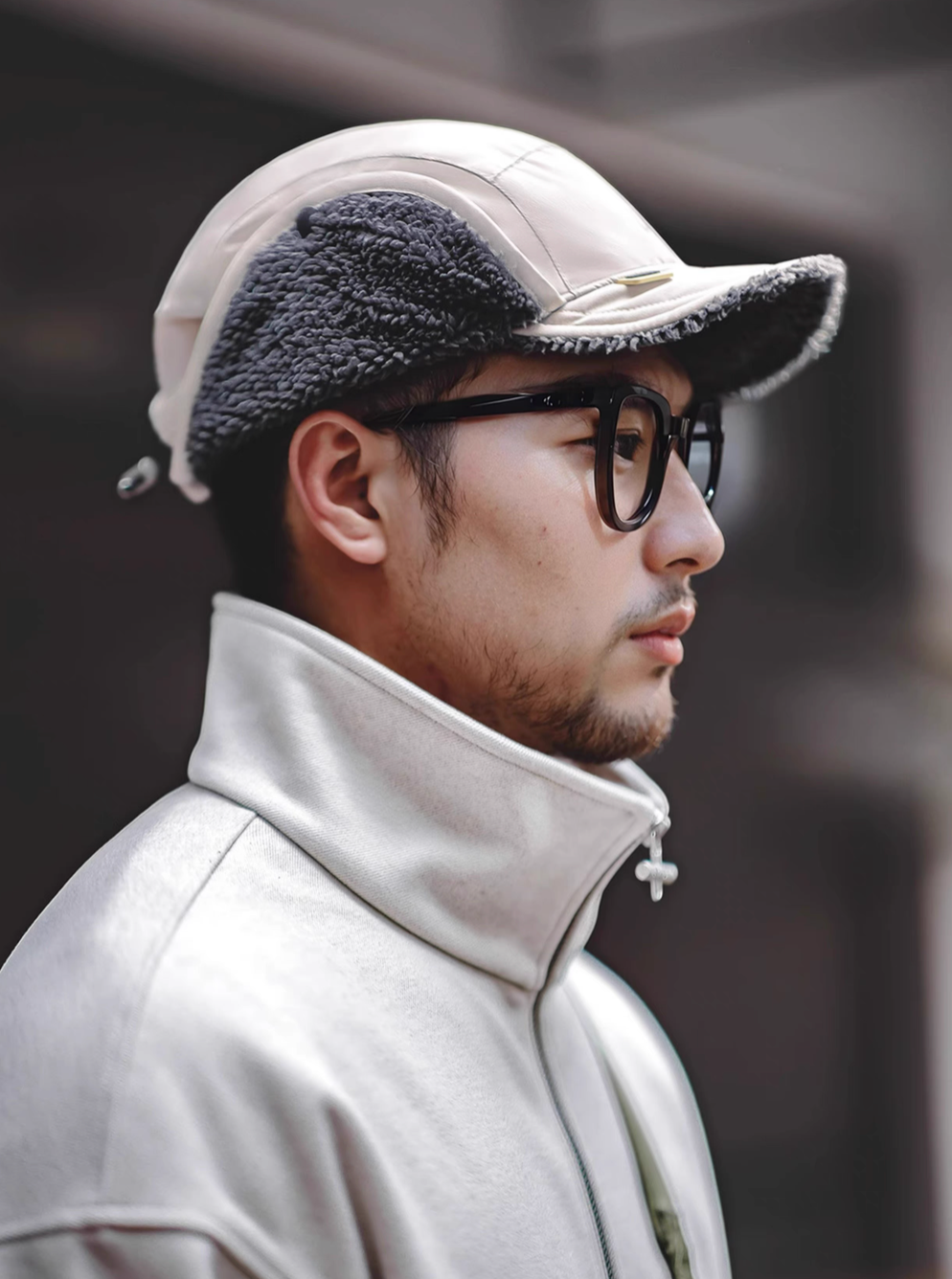 Side profile of Glacier Guard Fleece Cap mountain rock gray and white worn in city setting featuring short brim ear flaps and modern cold-weather look