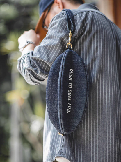Goal-Line Denim Sling Crossbody Bag denim blue worn over shoulder showing slim profile adjustable strap brass hardware and lightweight everyday carry design