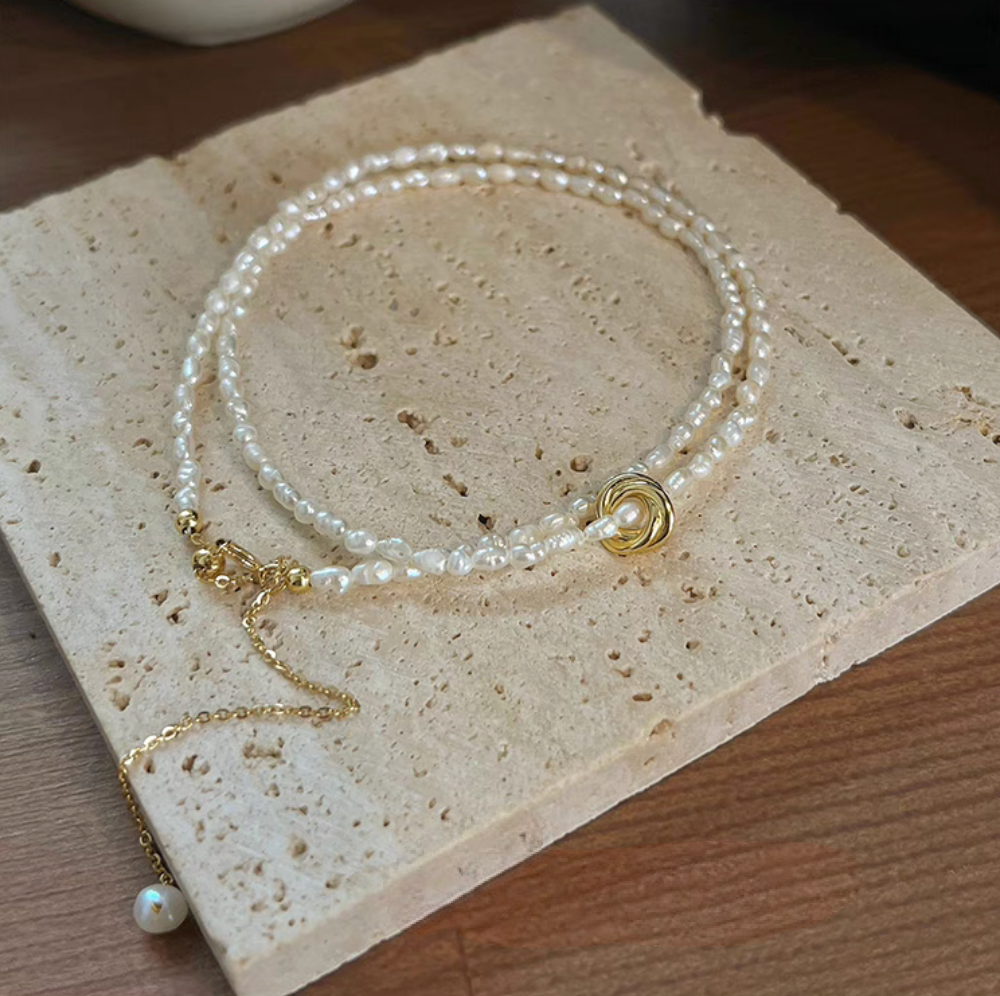 Golden Knot Freshwater Pearl Necklace with small natural pearls and gold knot centerpiece styled on stone surface