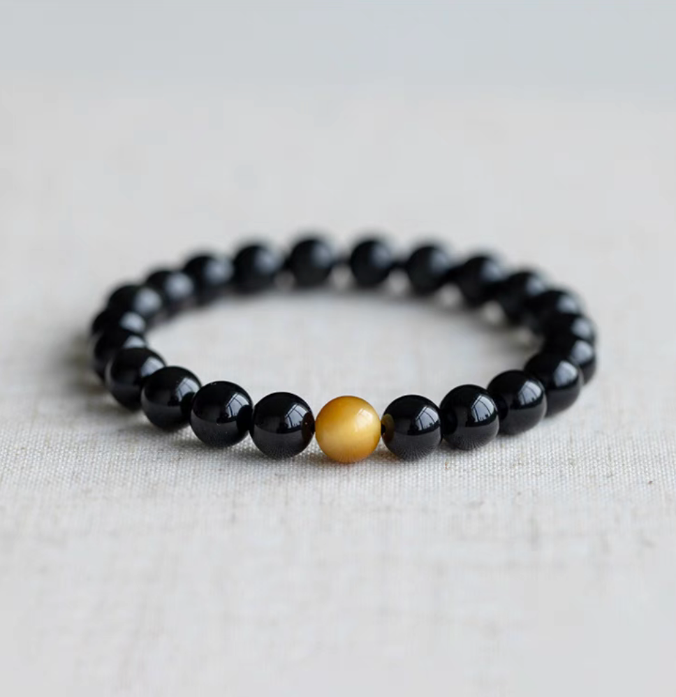 Golden tiger’s eye minimalist bracelet with black tiger’s eye beads and a single golden center bead displayed on neutral fabric background