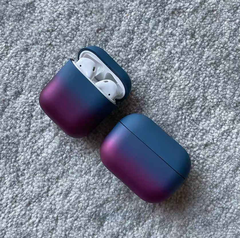 Peacock blue purple gradient AirPods case opened with earbuds inside alongside closed case on fabric background