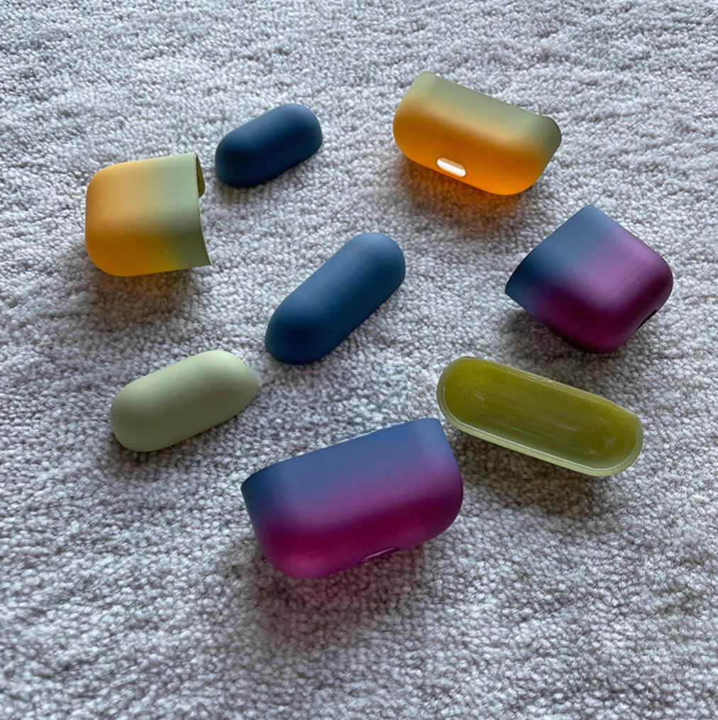 Multi-color gradient AirPods case set showing avocado green yellow and blue purple variations with separate case parts on textured carpet