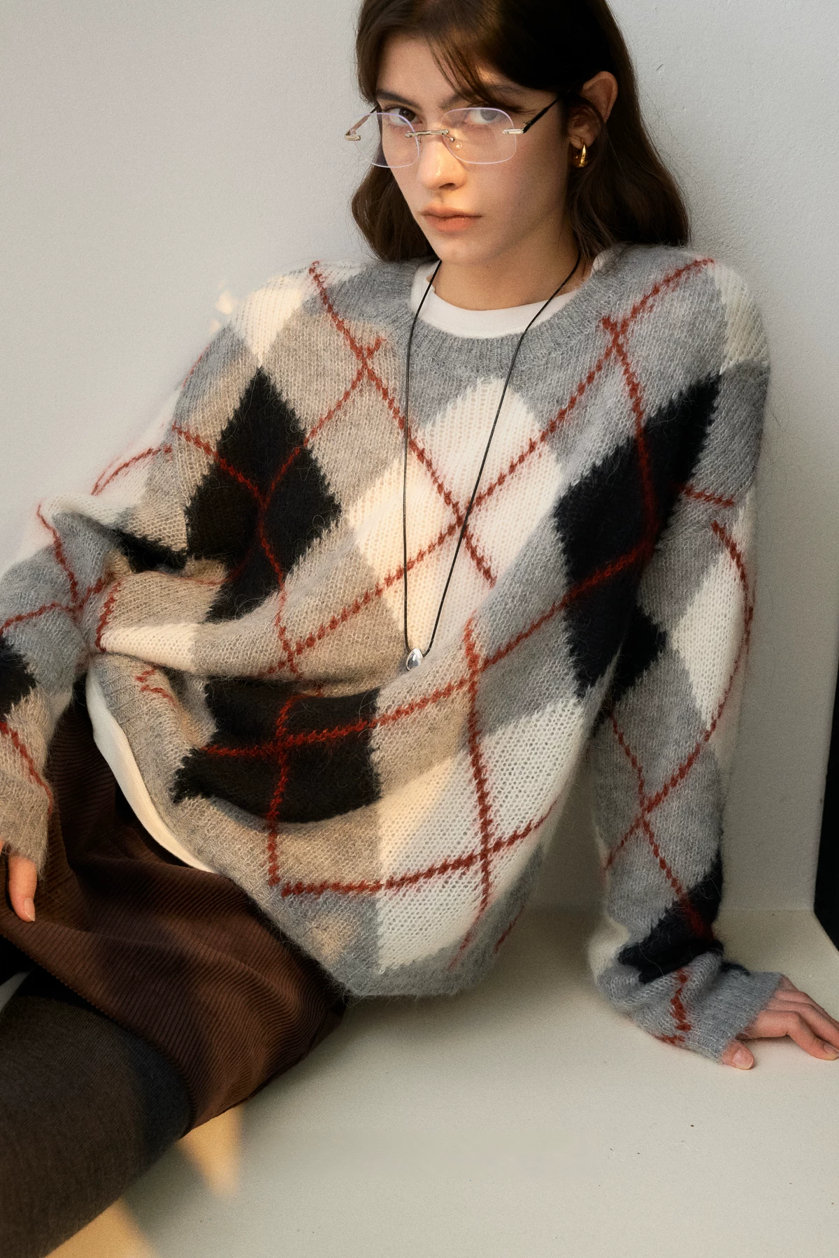Seated view of a Gray Argyle crewneck sweater with gray, cream, and black diamonds and rust overcheck