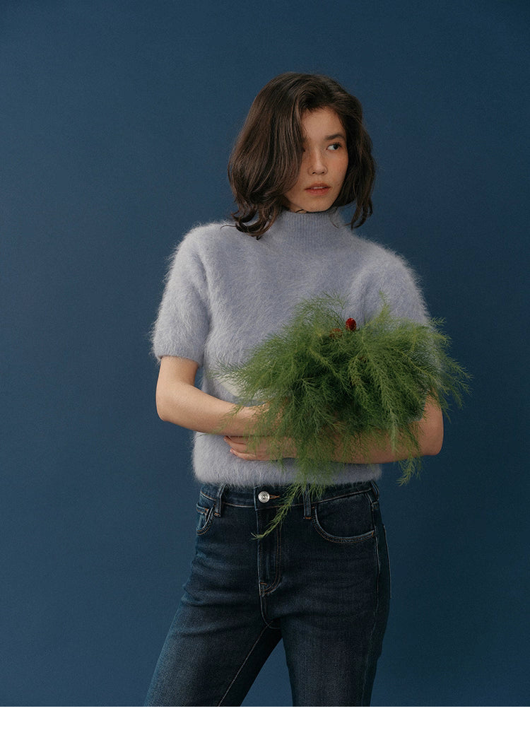 Full-body shot of the lavender HaloFuzz alpaca turtleneck tee with model raising her arms, paired with dark-wash jeans on a blue background.