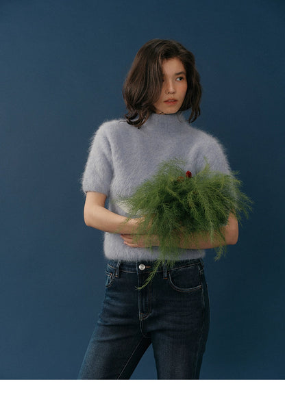 Full-body shot of the lavender HaloFuzz alpaca turtleneck tee with model raising her arms, paired with dark-wash jeans on a blue background.