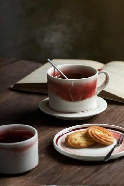 Beige and red handcrafted ceramic cup and saucer set used for tea with book and dessert creating a warm vintage coffee moment